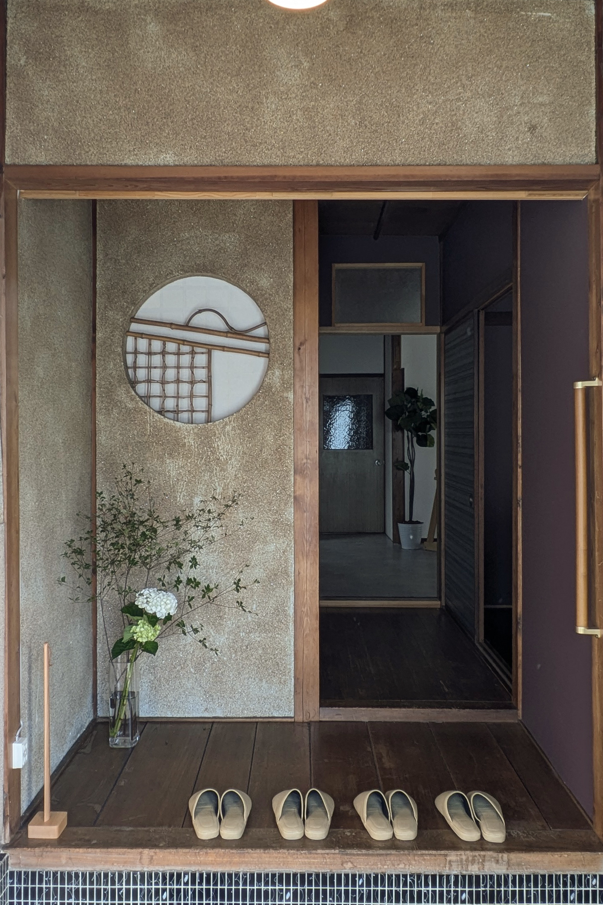百の宿の玄関。丸窓と竹格子、花活け。土間の奥に続く古民家の空間